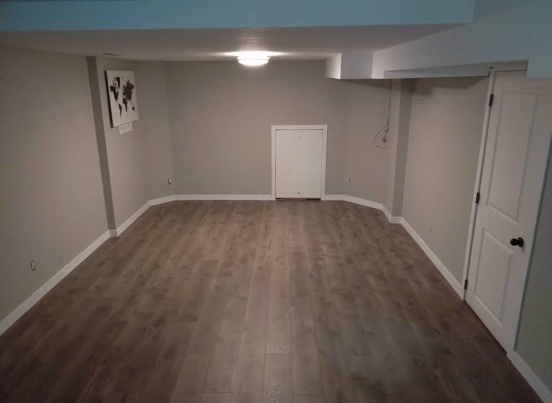 Finished basement with wood-look plank flooring and gray walls.