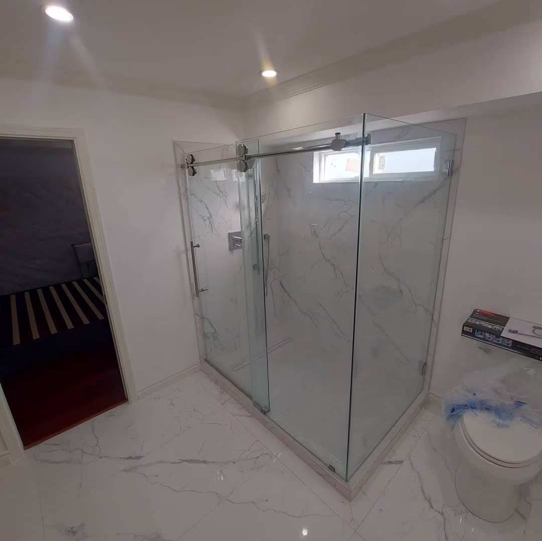 Glass corner shower enclosure with sliding doors in a marble-tiled bathroom.