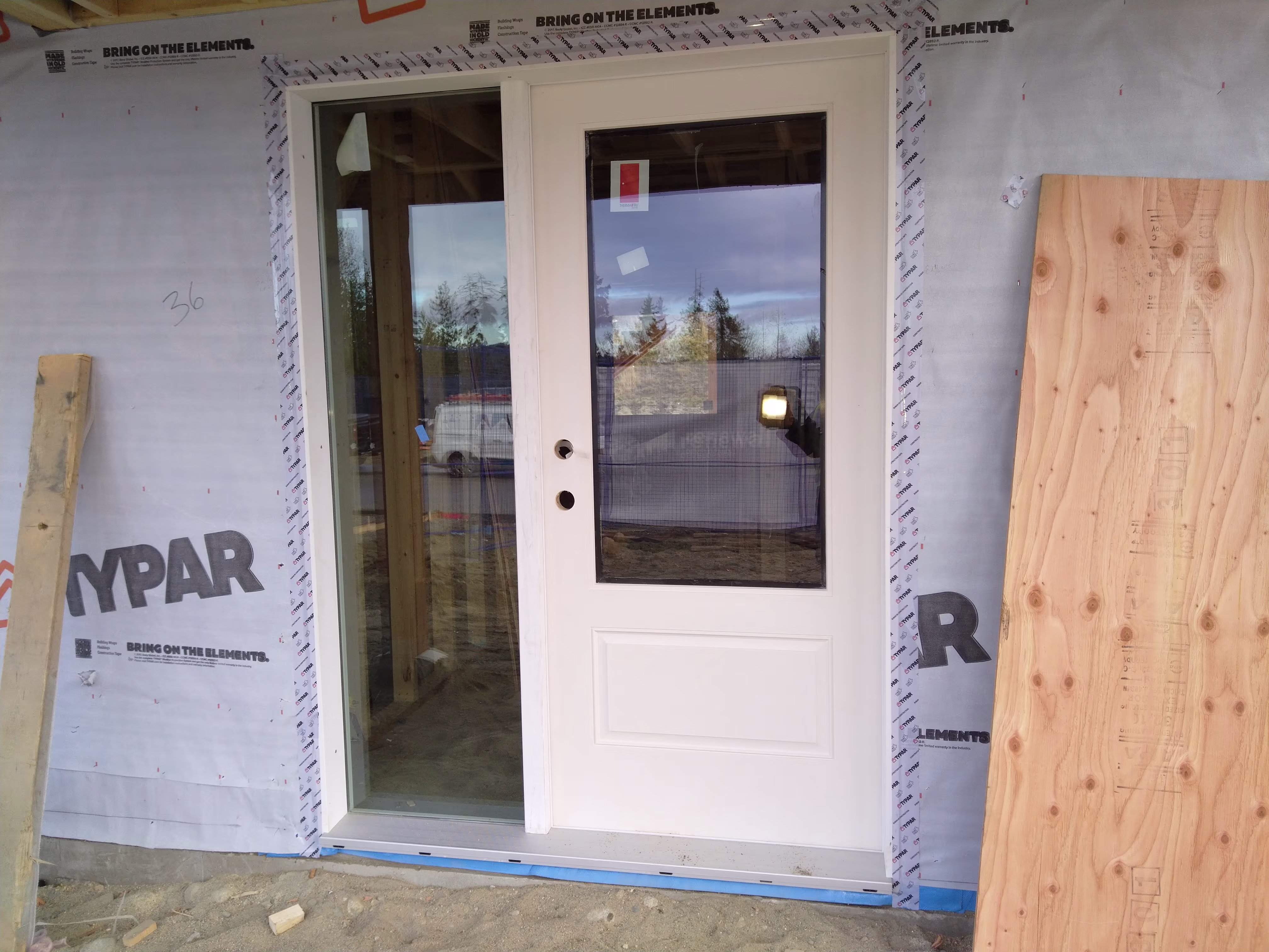 White exterior door with glass insert and sidelight being installed in a framed entry.