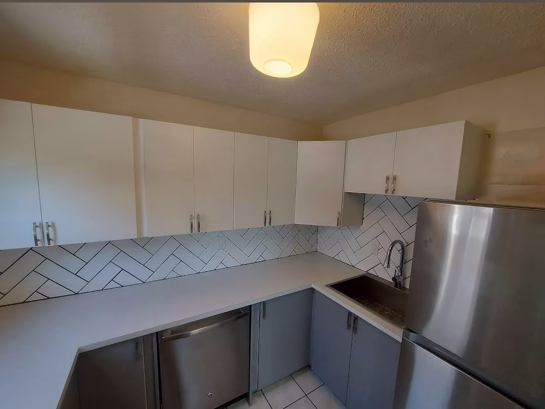 James Bay kitchen with white upper and gray lower cabinets, herringbone backsplash, and stainless fridge and sink.