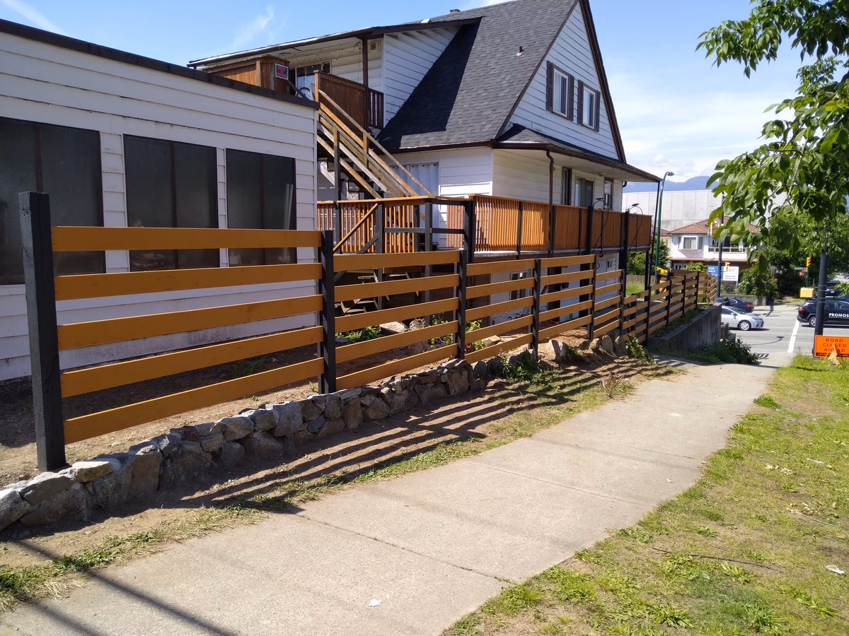 Horizontal wood slat fence with dark posts along a residential sidewalk