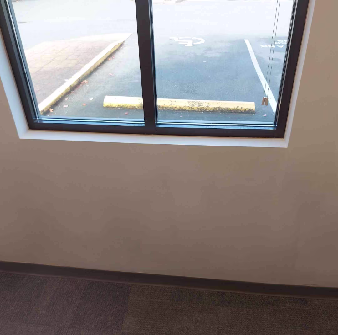Interior window with fresh white trim overlooking a parking lot and yellow wheel stop