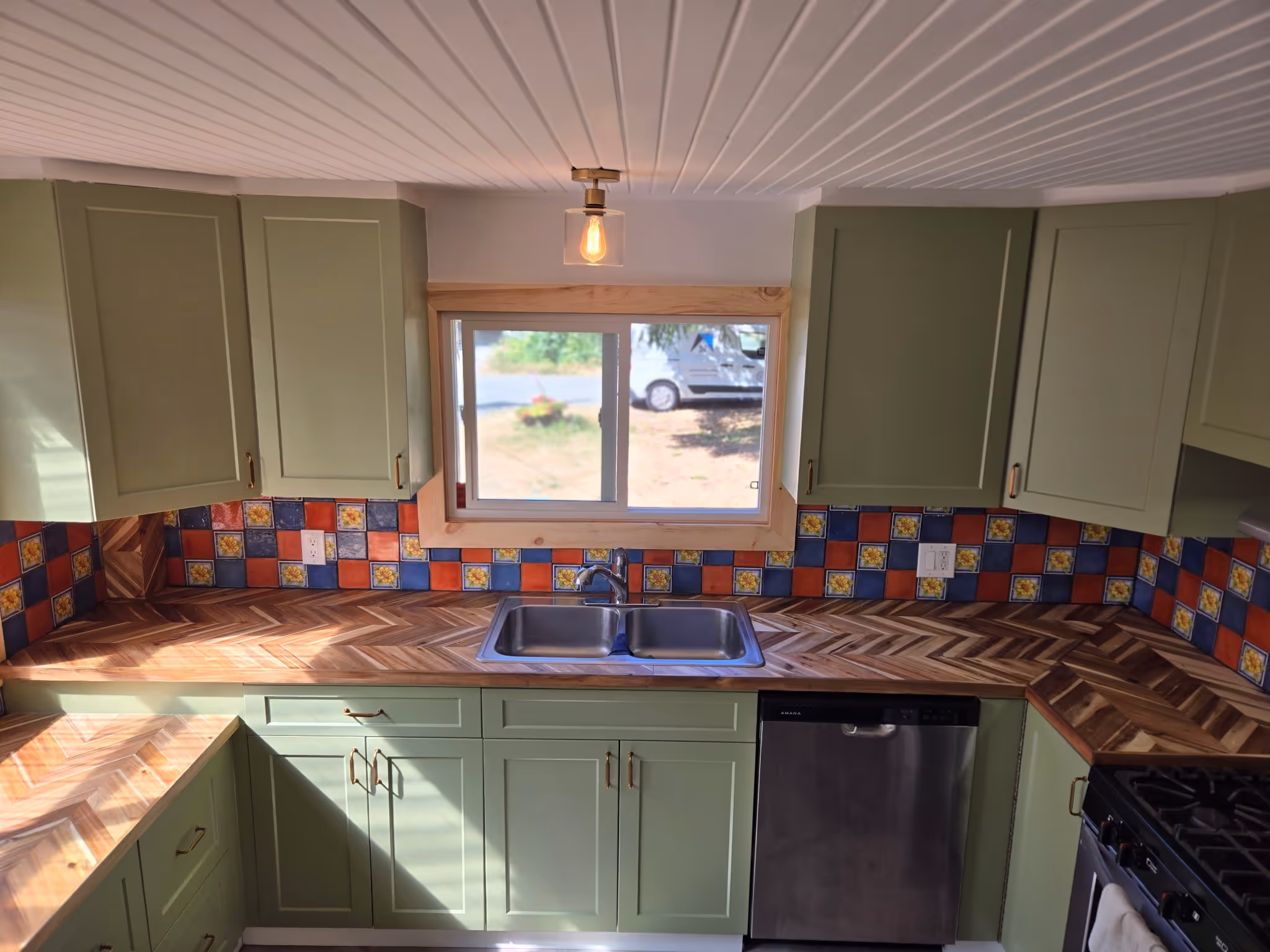 Kitchen with sage green cabinets, chevron wood countertops, and colorful tile backsplash.